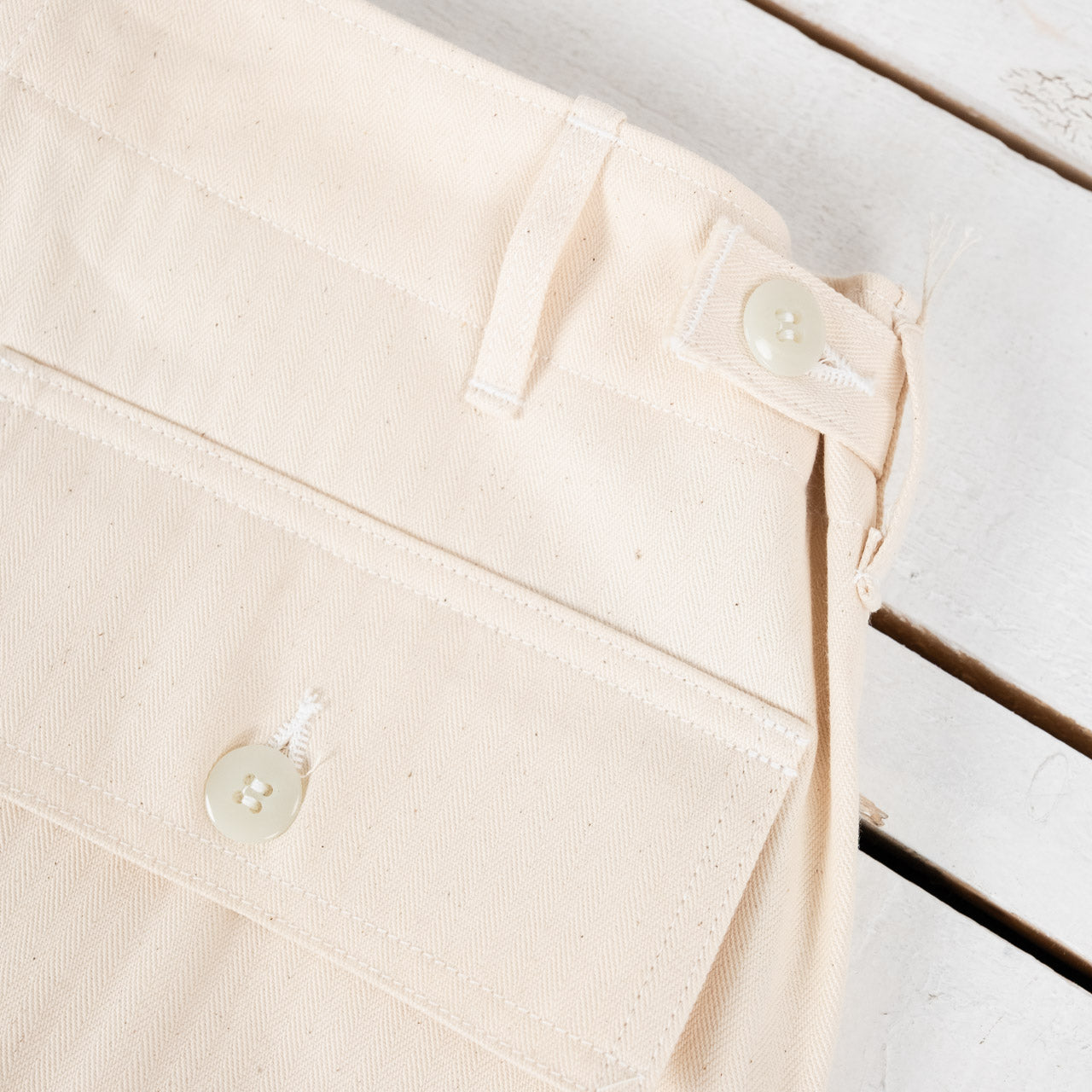 The Real McCoys Fatigue Pants in Ecru, Detailansicht des Hosenbunds mit Knopf und Lasche zur Weitenregulierung