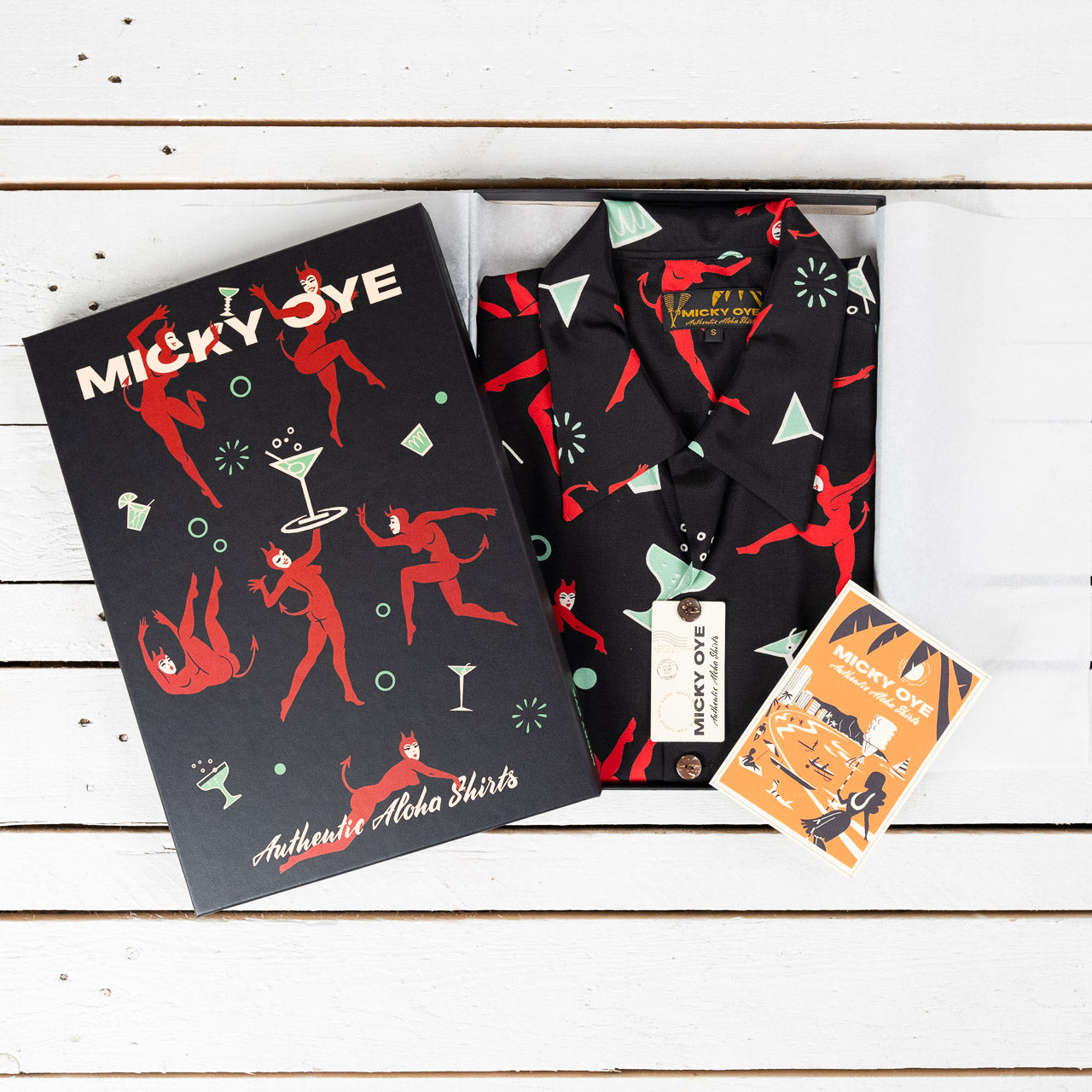 Micky Oye Aloha Shirt in Geschenkbox mit Retro-Teufel-Print und passendem Etikett – stilvoll verpackt auf weißem Holzhintergrund.