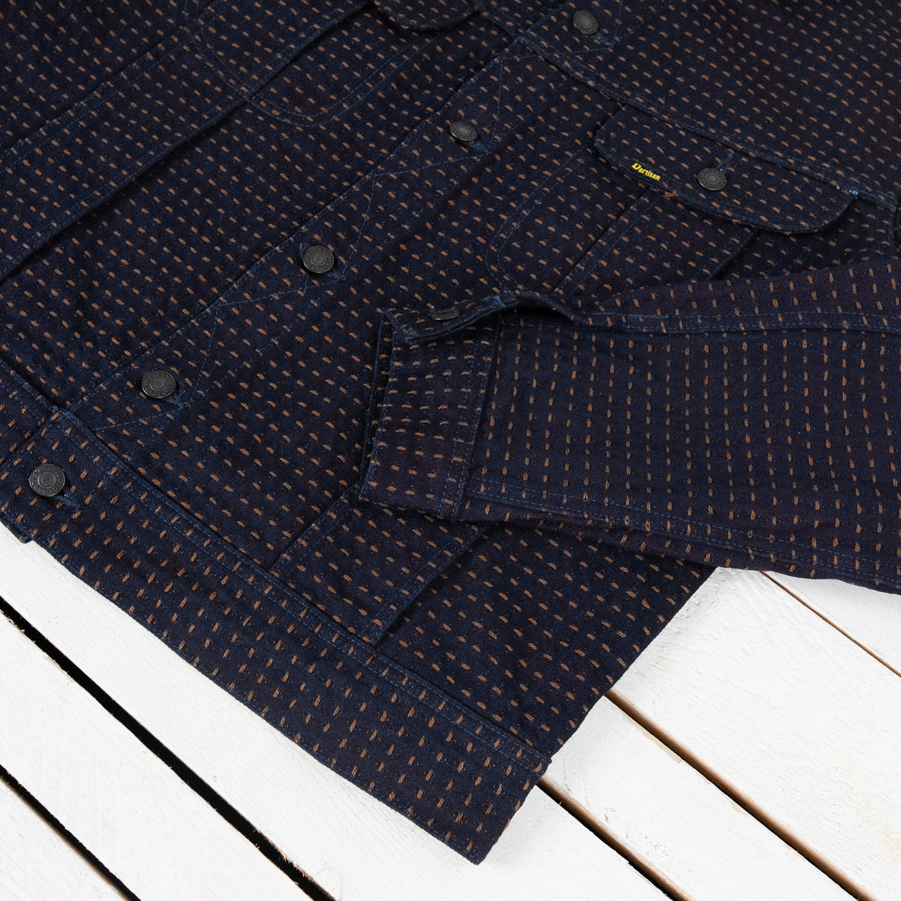 Studio D'Artisan Kakishibu Sashiko Denim Jacke in Indigo, Detailansicht der Knopfleiste und eines Ärmels, flach liegend auf weißem Untergrund