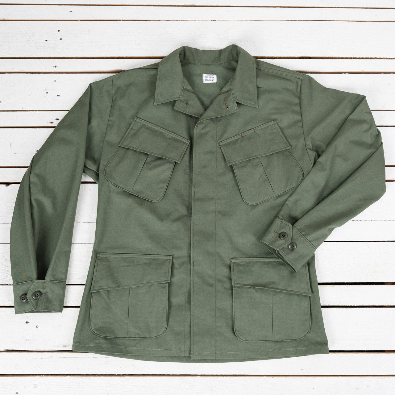 The Real McCoys Ripstop Jacke in Oliv, Ansicht von vorne, flach liegend auf weißem Untergrund